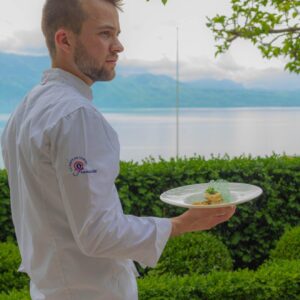 Vincent Buquet tenant une assiette sur une terrasse face au lac.